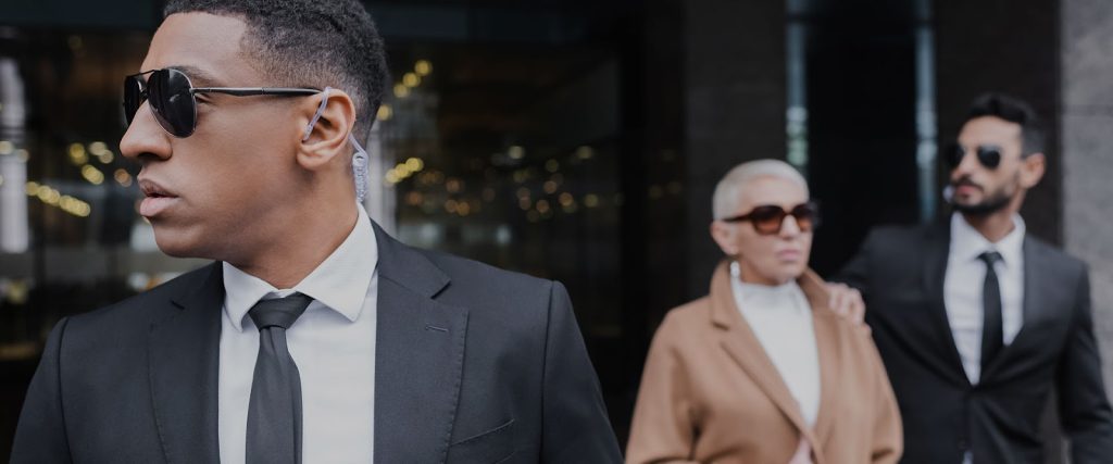 Women with two executive bodyguards protecting her outside a building